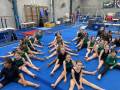 A group of children in lines stretching for gymnastics on a large blue mat.