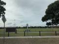 Image displays a green oval with a path, a fence and trees in the background. The sky is grey and overcast in this image