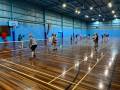 Adults on an indoor basketball court with a net playing pickleball.