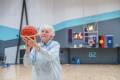 Phone of an older lady in a blue jumper holding a basketball about to take a shot at goal