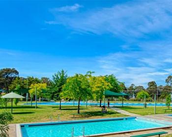 Serene park scene featuring glistening blue pools surrounded by lush greenery and vibrant trees under a bright blue sky.