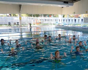 Aqua fitness class in a bright indoor pool, featuring participants immersed in water, focusing on exercise and movement.