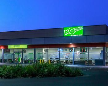 Exterior of a retail store at dusk, featuring a bright green "NO" sign and illuminated windows. 