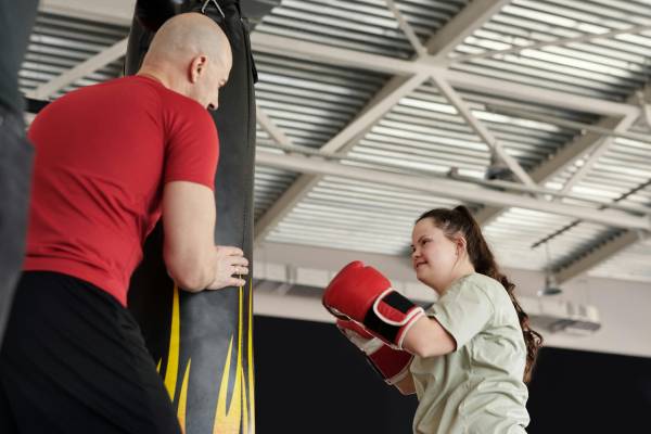 A girl boxing and a man holding the punching bag for her