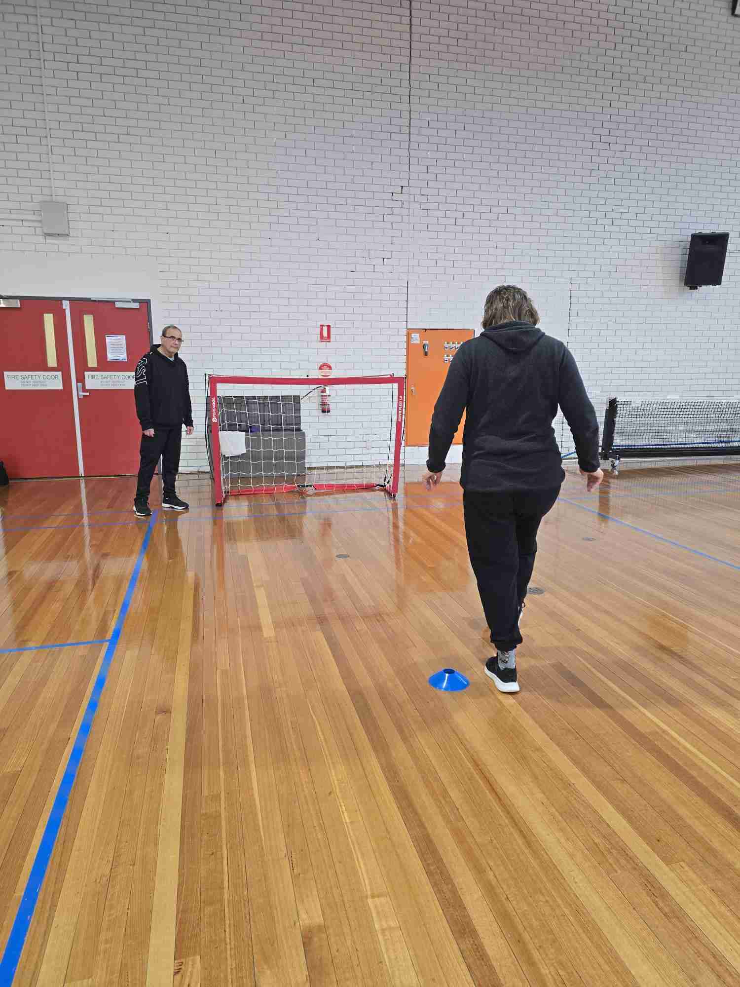 Two people on an indoor court with a pop up soccer net