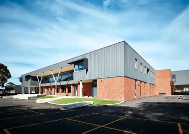 Modern two-story brick and metal commercial building with covered entrance, empty parking lot, and blue sky.